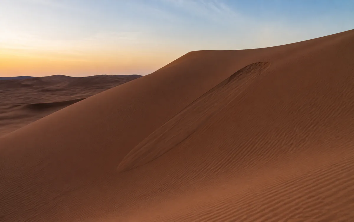 Wind-shaped desert dunes under a pale evening sky